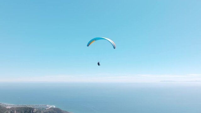Man with instructor flies with paraglide 4k, slow motion up in the air, cinematic aerial drone footage above Malibu USA. Extreme paraglider flying against a clear blue sky, sunbeam shines into camera