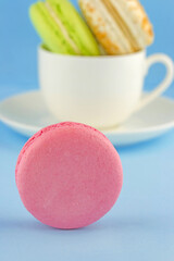 Close-up view of pink macaroon with white cup full of colorful macaroons behind