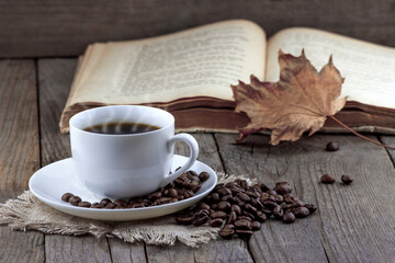 White cup of coffee with autumn leaf and old book on wooden background