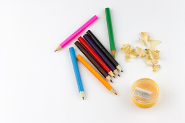 Top view of school supplies colored pencils, sharpener and pencil shavings on white background
