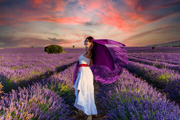 Woman looking at the camera while posing outdoors in a colorful lavender flower field at sunset.