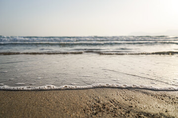 foamy bubble waves crashing gently from the sea to the beach at sunset, selective focus