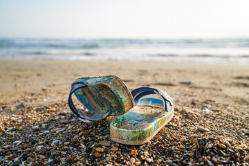 focused colorful and sandy kids slippers sandals is on the beach, sunset and wavy sea,  the sea and...