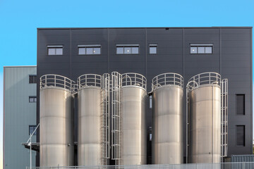 chrome silos in front of generic grey wall of a plant
