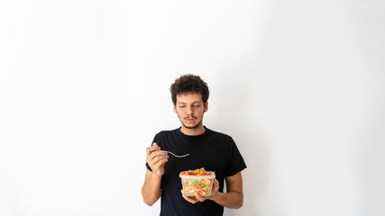 Happy young caucasian man eating and holding a healthy mediterranean pasta salad tupperware