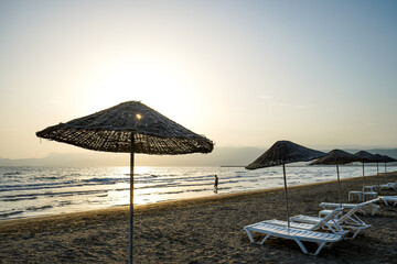 people walks on beach at sunset, lounge chair, beach umbrella parasol, tanning bed
