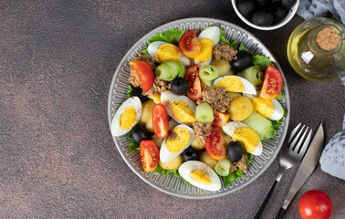 French salad Nicoise with tuna, boiled potatoes, egg, black olives, cucumbers, tomatoes and lettuce, Top view on brown background