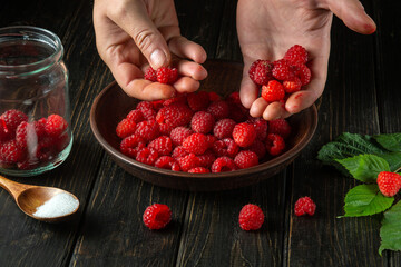 The cook is sorting through fresh red raspberries in the kitchen to prepare a sweet soft drink. Cooking diet desserts.