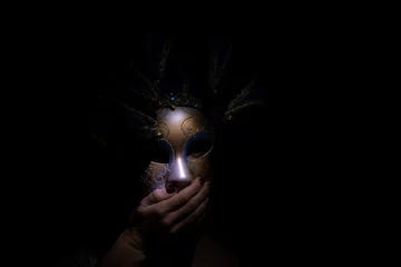 Foto op Plexiglas The face of a girl in a Venetian carnival mask in the dark covers her mouth with her hand, a masquerade and an actor in a mask, a mystery © Виктория Котлярчук
