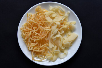 Salted squid appetizer for beer on a white plate. Delicious straws of spicy squid on a black background.