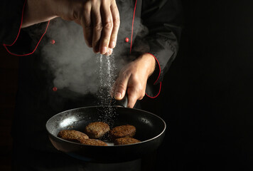 Professional chef adds salt to cutlets that are fried in a pan. Cooking meat patties for a burger....