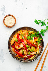 Asian cuisine, stir fry with chicken, red paprika pepper and zucchini bowl. White kitchen table background, top view, copy space