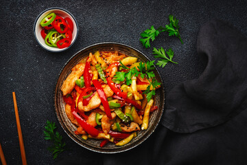 Asian cuisine, stir fry with chicken, red paprika pepper and zucchini bowl. Black kitchen table background, top view, copy space