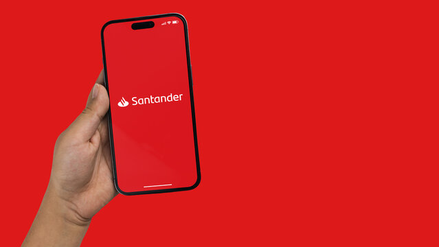 Boy holding a smartphone iPhone 14 Pro with Santander bank app app on the screen. Red background. Rio de Janeiro, RJ, Brazil. September 2022