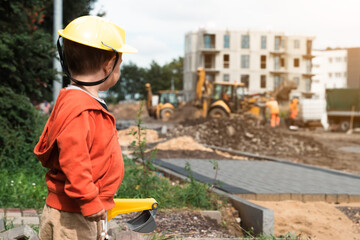 Child with excavator near construction site, dreams to be an engineer. Little builder. Education, and imagination, purposefulness concept - 534595207