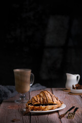 Croissant with chocolate on a wooden table, a glass of cappuccino or coffee, delicious breakfast and sweets, healthy food view from above, bun and milk chocolate