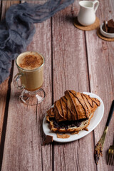 Croissant with chocolate on a wooden table, a glass of cappuccino or coffee, delicious breakfast and sweets, healthy food view from above, bun and milk chocolate
