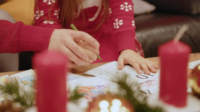 Little girl draw at the table near the fireplace and the Christmas tree. Cute child paints a picture with a pen at home. Little girl draw a picture for santa in New Year in the room. Profile view