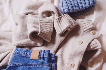 Trendy woolen cardigan, fancy jeans and blue knitted hat. Fashionable winter women's clothing. Warm clothes flat lay photography