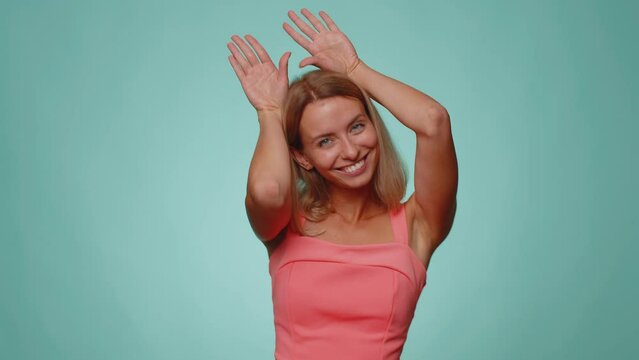 I am little bunny rabbit. Lovely funny young woman smiling friendly and doing bunny ears gesture on head, having fun, fooling with humorous comical mood. Girl isolated alone on studio blue background