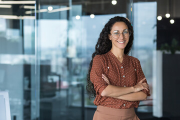 Portrait of a young beautiful Hispanic woman. Curly Latin American student in glasses stands in the...