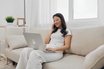 Asian Millennial woman sitting with laptop and talking on phone freelance student with looking at laptop screen working, lifestyle work and home