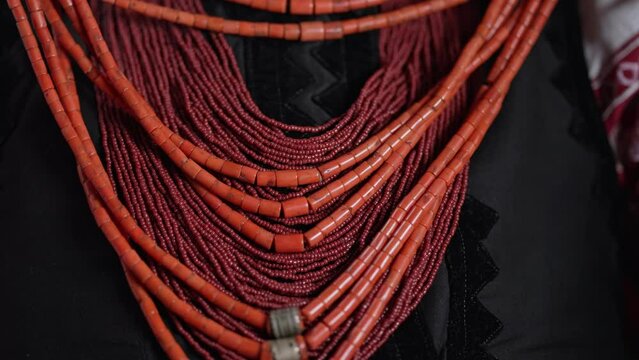 Ukrainian woman puts on authentic jewelry - coral beads. She is in national costume of Ukraine - vyshyvanka. Folk handmade necklace in traditional style.
