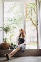 A young woman sits by the window in her flower shop. Small business concept.