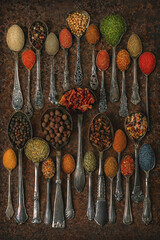 Various spices, condiments in vintage spoons on a dark retro background.