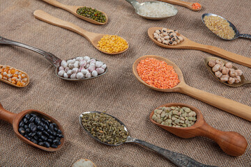 Vegan protein source. Various kinds of legumes, lentils, chickpeas and beans in different spoons on wooden table. top view.