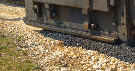 CLOSE UP: Laying black asphalt over crushed rocks with asphalt paver machine