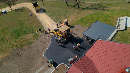AERIAL: Group of construction workers laying asphalt concrete on yard and road