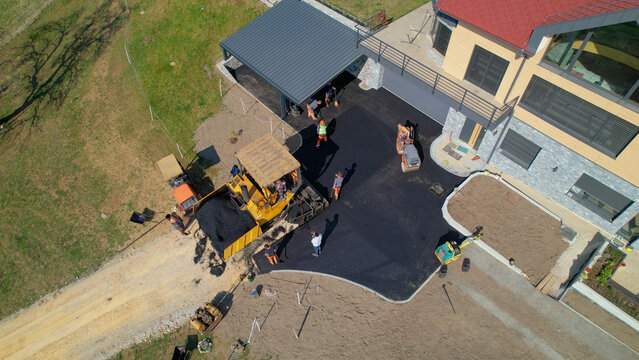 AERIAL: Builders smoothing and levelling asphalt surface yard in morning light