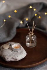 Liquid home fragrance with burning scented candle on stone tray over glow christmas lights at home close up. Cozy hygge atmosphere with candlelight.