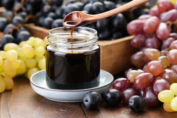 Jar of grape molasses, grape syrup. Sweetener, cough medicine. Black, green and purple grapes on...
