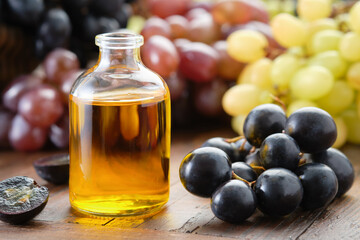Organic grape seeds essential oil bottle. Black, green and purple grapes on table.