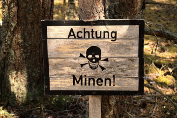 Caution, mines! warning sign in German language with skull on mined area. 