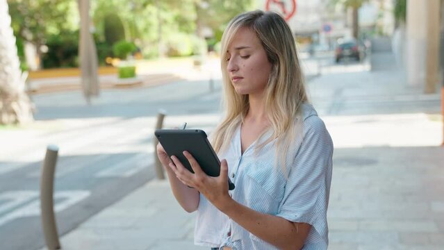 Young blonde woman drawing on touchpad with serious expression at street