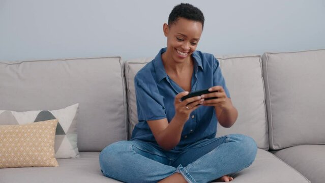 African american woman playing video game by smartphone at home