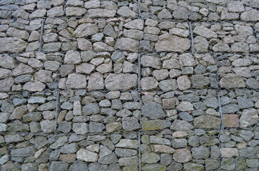 A pile of stones form a wall, contained by some wires