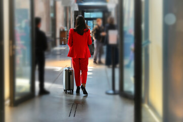 Unrecognizable elegant red dressed woman backview walking out hotel lobby carrying trolley