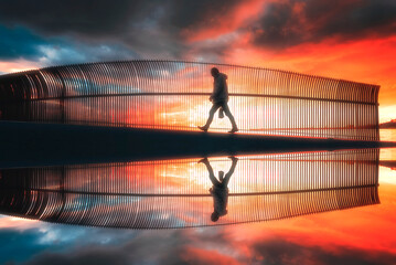 Solo male walking on a bridge with sunset and colorful sky at background and reflection