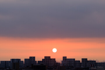Fototapeta premium 兵庫県神戸市東灘区の高層マンションの上層階からの夜明け。大阪生駒山から太陽が昇り、あたりはオレンジ色に染まり、ビル群がシルエットで浮かぶ