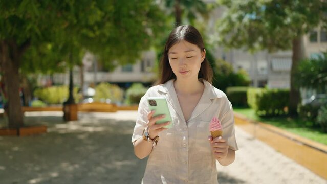 Chinese woman using smartphone eating ice cream walking at park