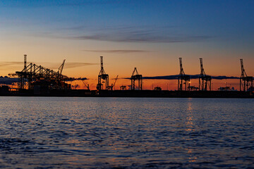 Fototapeta na wymiar Panoramic image of the cargo port at sunset. Gdansk at night with container terminals, cargo cranes at sea and clear blue sky. Cargo sea port