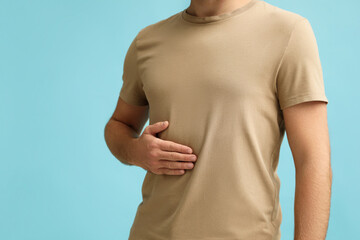 Man holding hand near body against turquoise background, closeup. Space for text