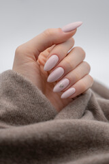 Single female hand on a soft cozy wool sweater blanket - modern pink nails with glitter heart polish design - slim manicured fingers