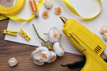 Hot glue gun and handicraft materials on wooden table, flat lay