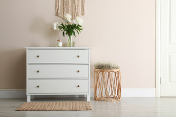 Room interior with white chest of drawers near beige wall. Space for text
