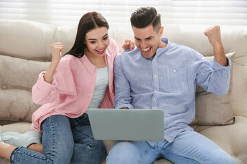Emotional couple participating in online auction using laptop at home - obrazy, fototapety, plakaty